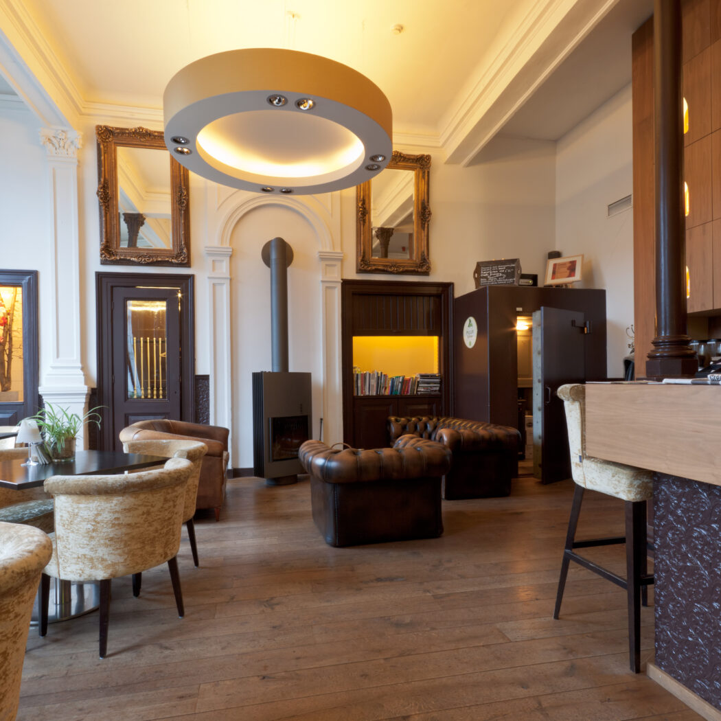 Sfeervolle hotellounge met houten vloer, Chesterfield-zitjes, moderne open haard en bar met verlichte wijnflessen.
