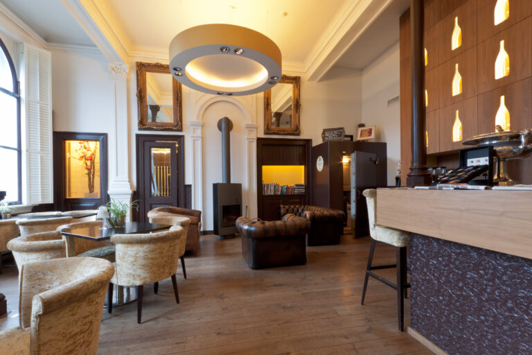 Sfeervolle hotellounge met houten vloer, Chesterfield-zitjes, moderne open haard en bar met verlichte wijnflessen.