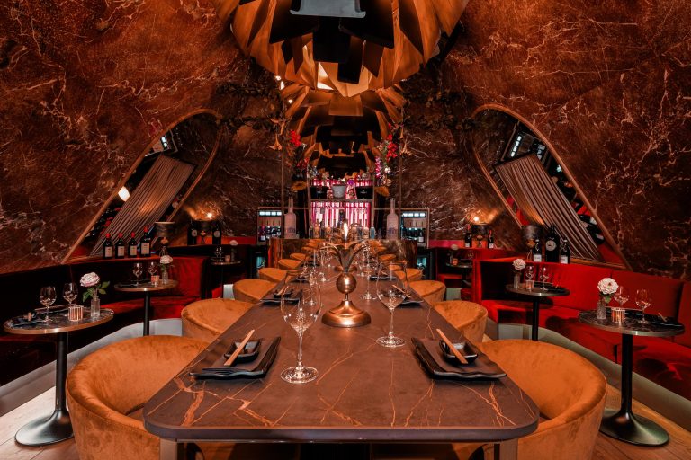 Luxe restaurant interieur met een lange donkere eettafel, oranje fluwelen stoelen en bruin marmeren wanden.