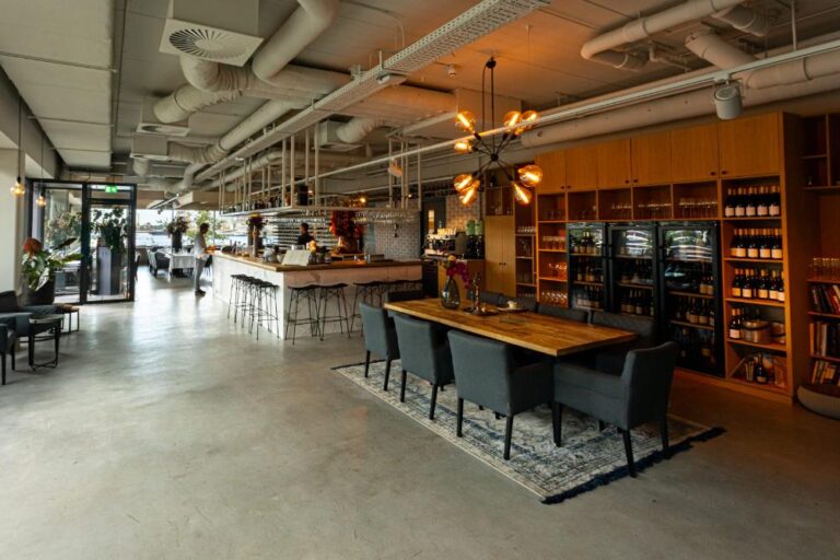 Ruim, modern restaurant met houten bar, lange eettafel en een wand vol wijnen.