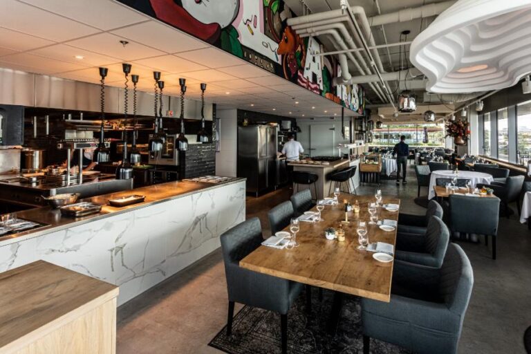 Stijlvol restaurantinterieur met open keuken, marmeren bar, houten tafels en een kleurrijke muurschildering.