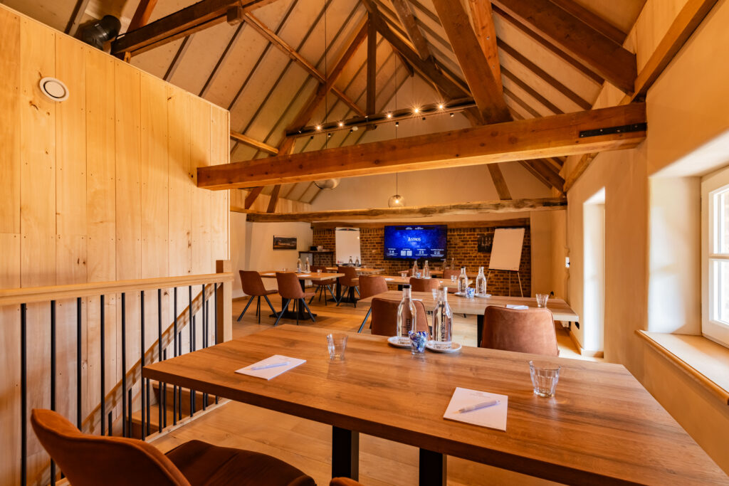 Ruime vergaderruimte met houten balkenplafond, tafels, bruine stoelen en tv-scherm met Astros.