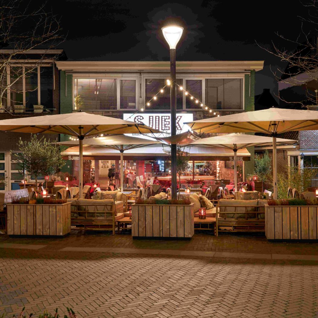 s Nachts verlicht terras van restaurant SJIEK met grote parasols, sfeervolle lichtslingers en comfortabele loungebanken.