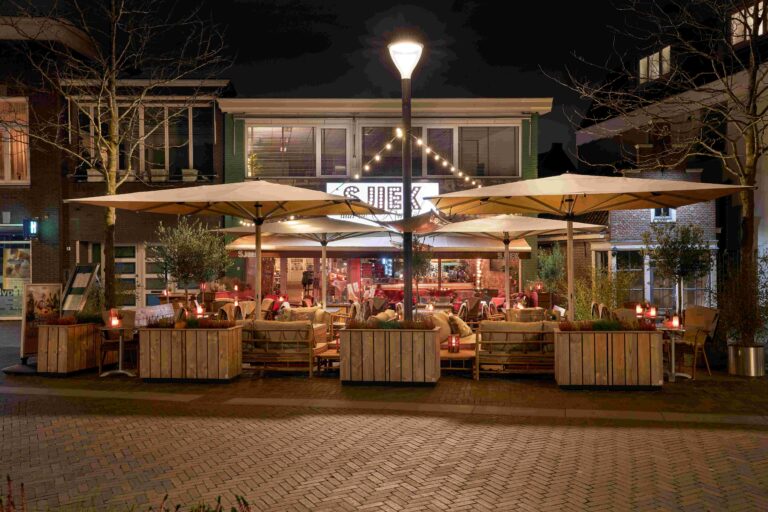 s Nachts verlicht terras van restaurant SJIEK met grote parasols, sfeervolle lichtslingers en comfortabele loungebanken.