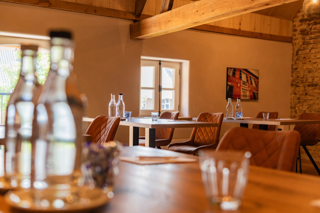 Sfeervolle vergaderruimte met houten tafels, bruine stoelen, waterflessen en glazen bij natuurlijk licht.