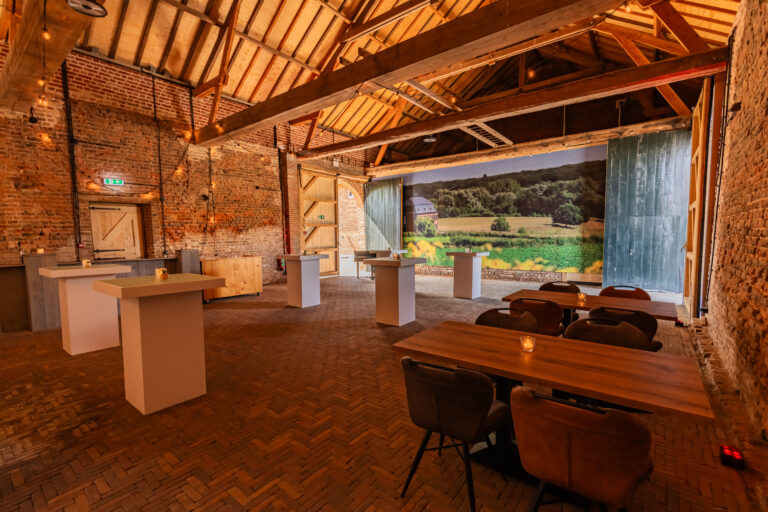 Sfeervolle evenementenlocatie in een rustieke schuur, ingericht met diverse tafels en een landschapsmuurschildering.
