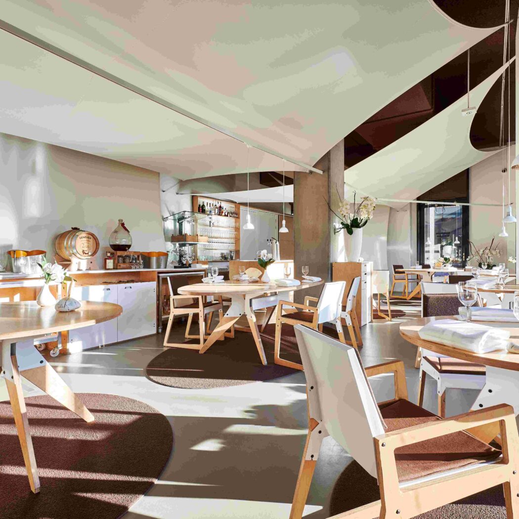 Modern en licht restaurant met ronde houten tafels, designstoelen en sfeervolle witte plafonddoeken.