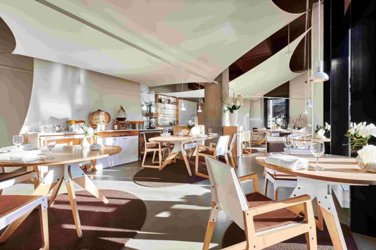 Modern en licht restaurant met ronde houten tafels, designstoelen en sfeervolle witte plafonddoeken.