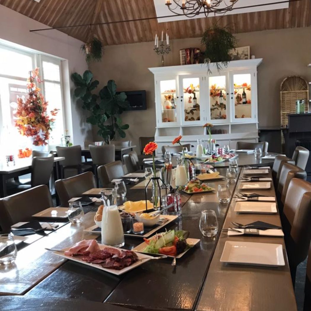 Lange, gedekte tafel in een lichte restaurantzaal met houten plafond en herfstdecoraties, klaar voor brunch.