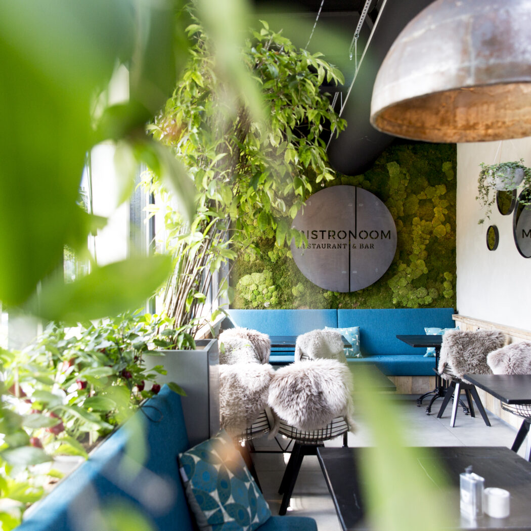 Sfeervolle inrichting van BISTRONOOM RESTAURANT & BAR met moswand, blauwe banken, stoelen met vachtjes en industriële lamp.