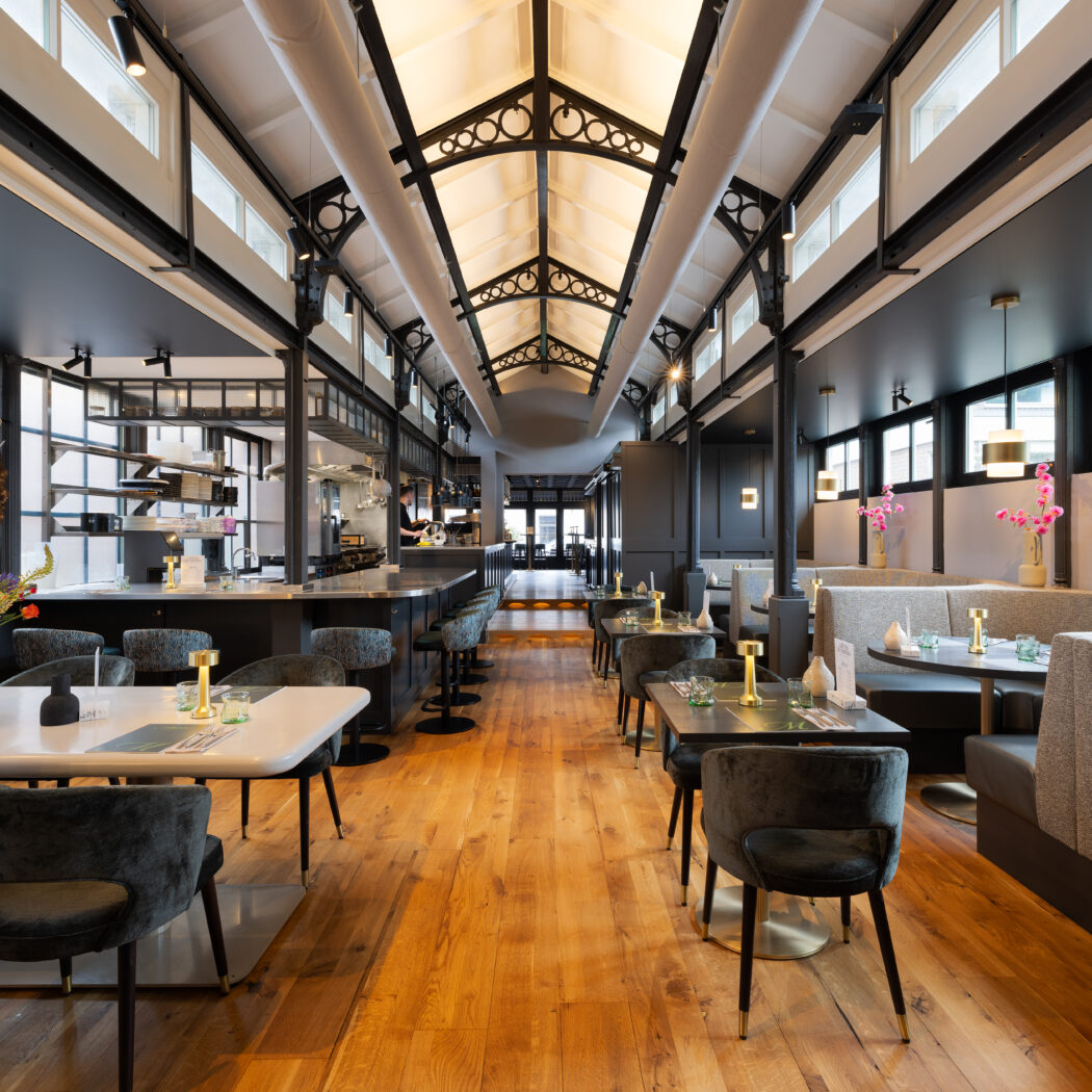 Stijlvol restaurantinterieur met een langwerpige zaal, hoge gewelfde plafonds, houten vloer en diverse zitplaatsen.