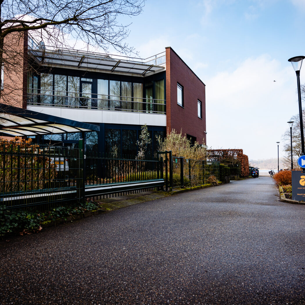 Bakstenen gebouw met glazen gevel en oprit, naast een bord voor Aan de Poel valet parking.