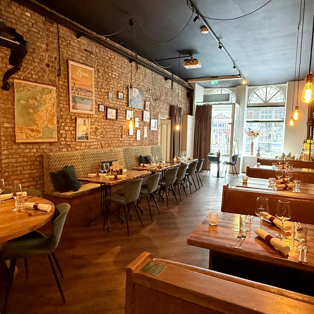 Restaurant interieur: houten tafels, stoelen en banken in een ruimte met bakstenen muren en wijnrek.