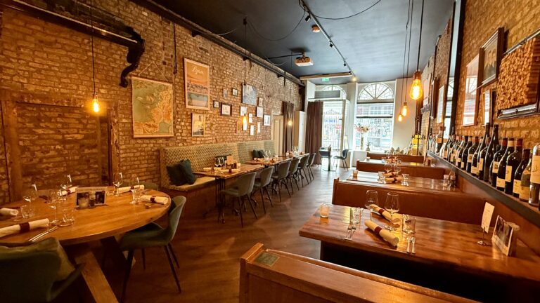 Restaurant interieur: houten tafels, stoelen en banken in een ruimte met bakstenen muren en wijnrek.