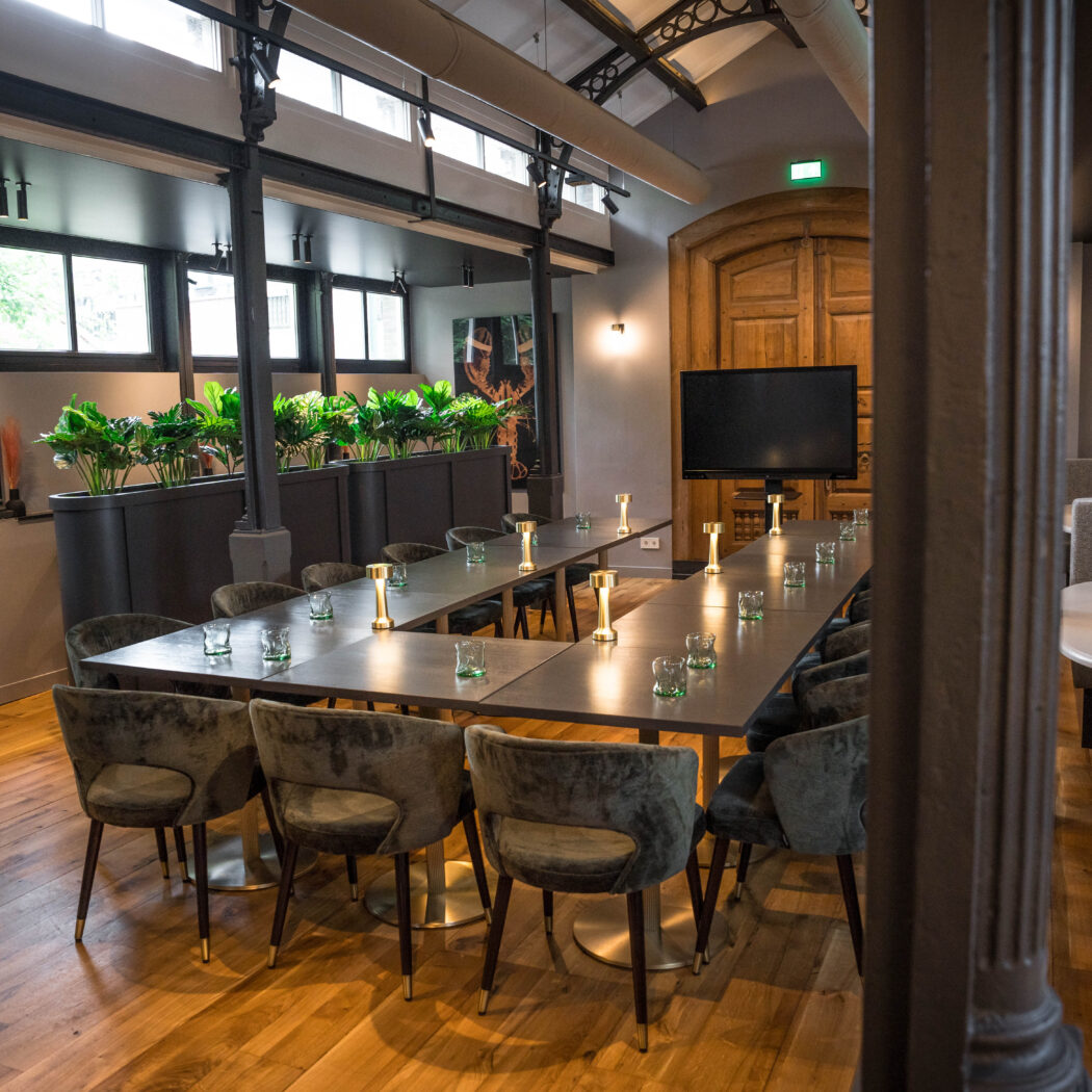 Sfeervolle, moderne vergaderruimte met lange U-vormige tafel, donkergrijze stoelen, tv-scherm en planten.
