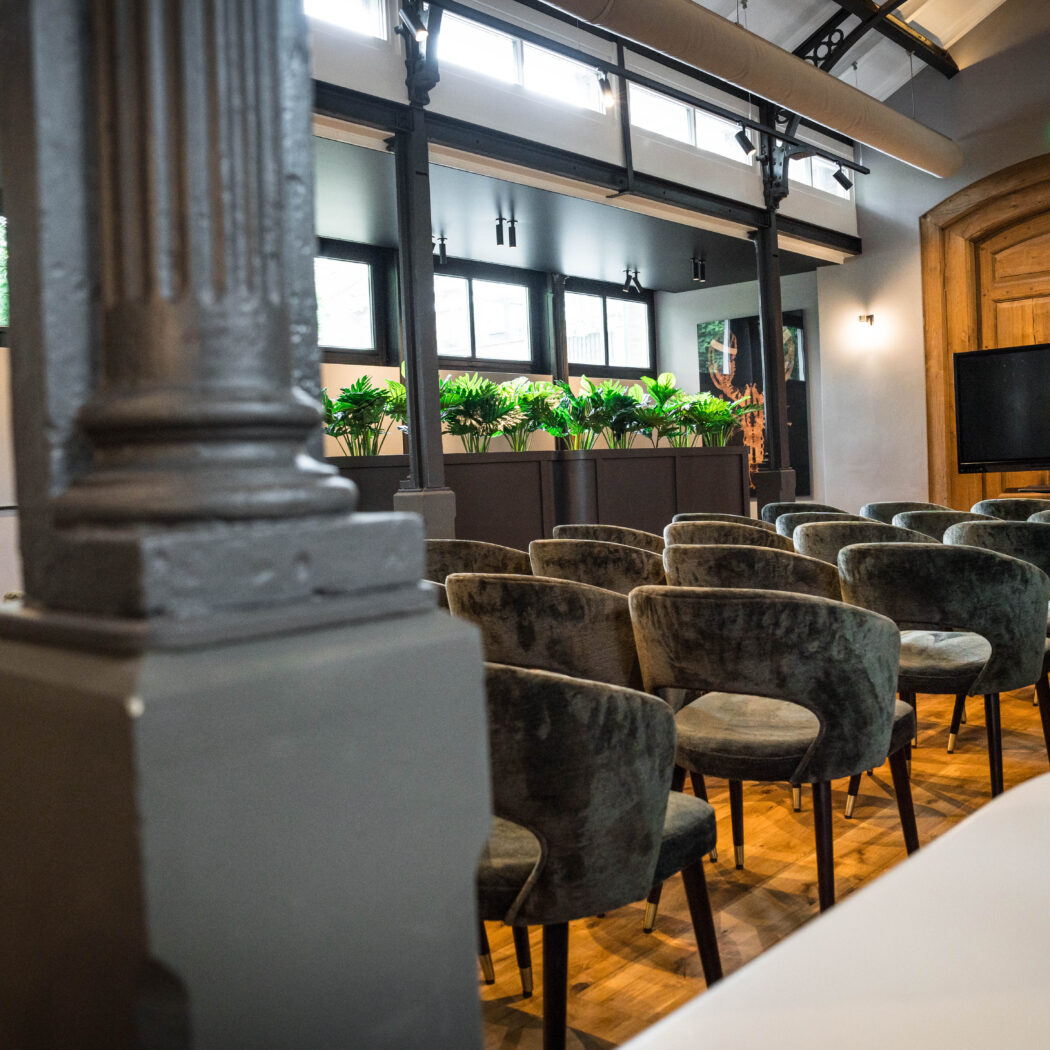 Elegante evenementenruimte met rijen donkergroene fluwelen stoelen, een tv-scherm en decoratieve planten.