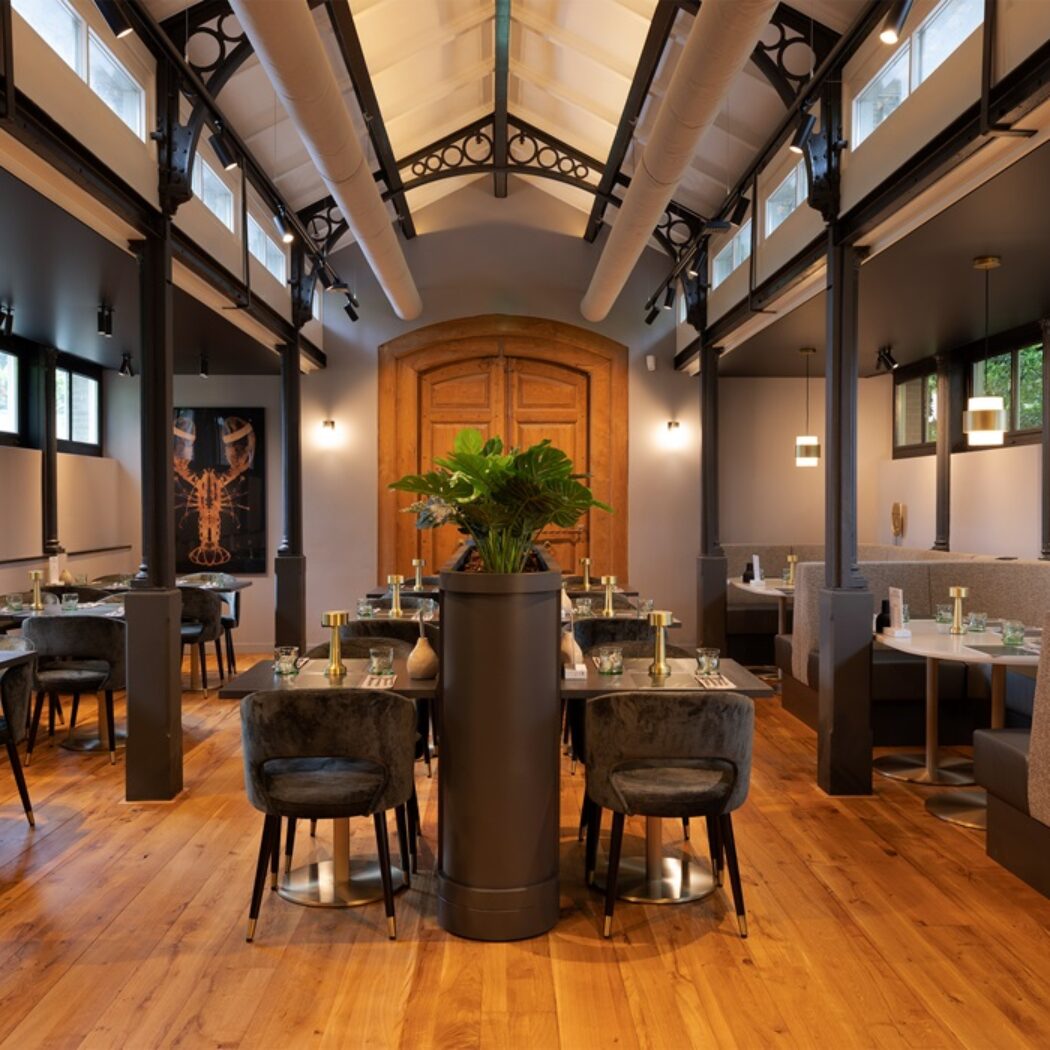 Sfeervol restaurant met houten vloer, hoge plafonds met donkere balken, velvet stoelen en comfortabele zitbanken.