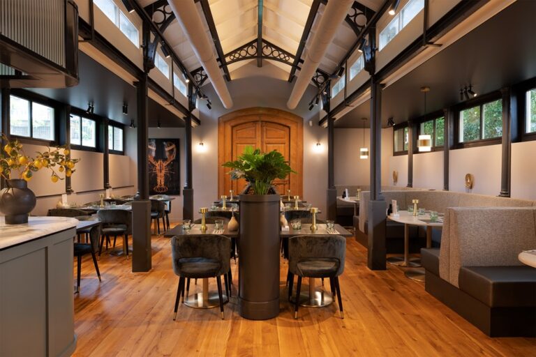 Sfeervol restaurant met houten vloer, hoge plafonds met donkere balken, velvet stoelen en comfortabele zitbanken.