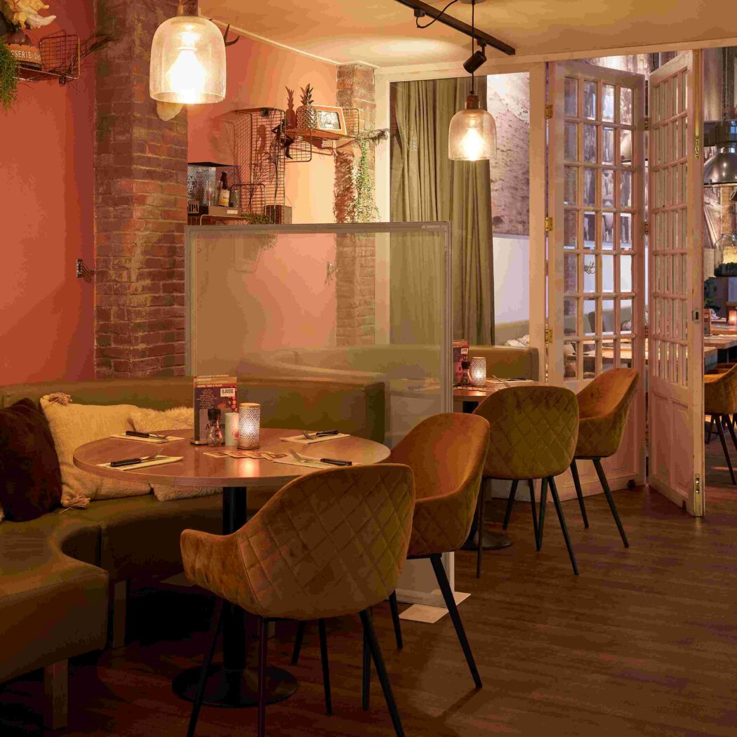 Knus restaurantinterieur met olijfgroene zitbanken, amberkleurige stoelen en sfeervolle verlichting.