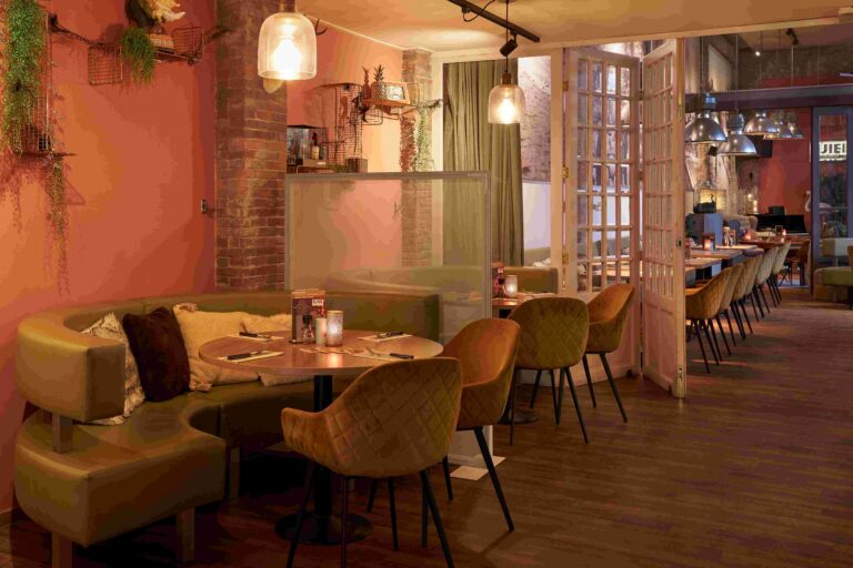 Knus restaurantinterieur met olijfgroene zitbanken, amberkleurige stoelen en sfeervolle verlichting.