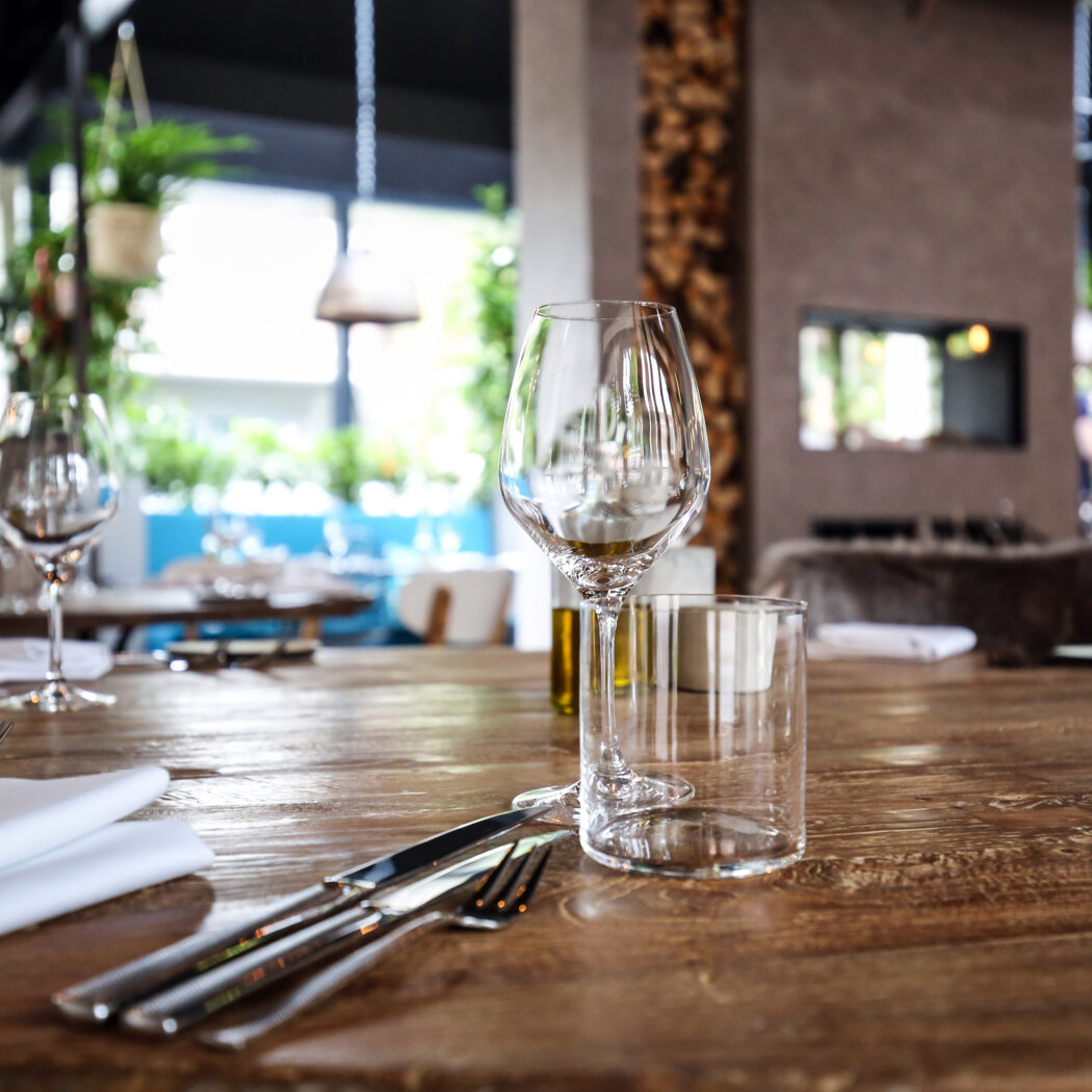 Gedekte rustieke houten restauranttafel met wijnglas, waterglas en bestek in een stijlvol interieur.