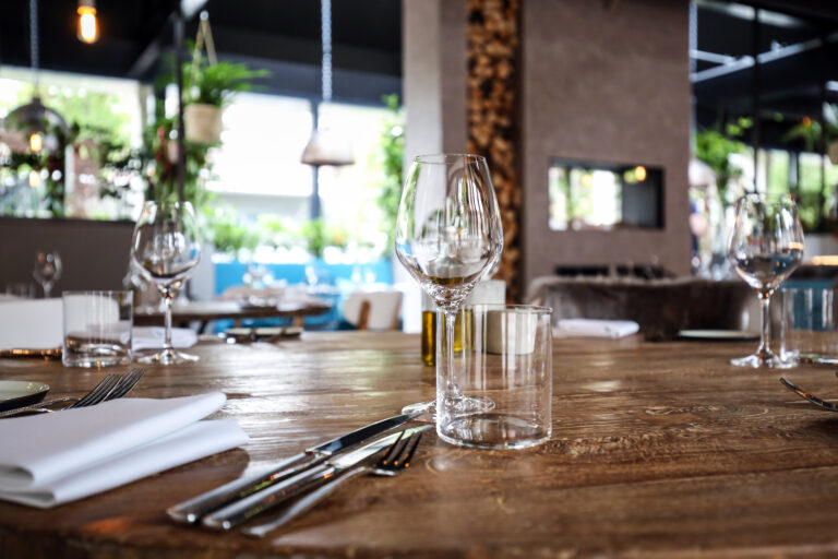 Gedekte rustieke houten restauranttafel met wijnglas, waterglas en bestek in een stijlvol interieur.