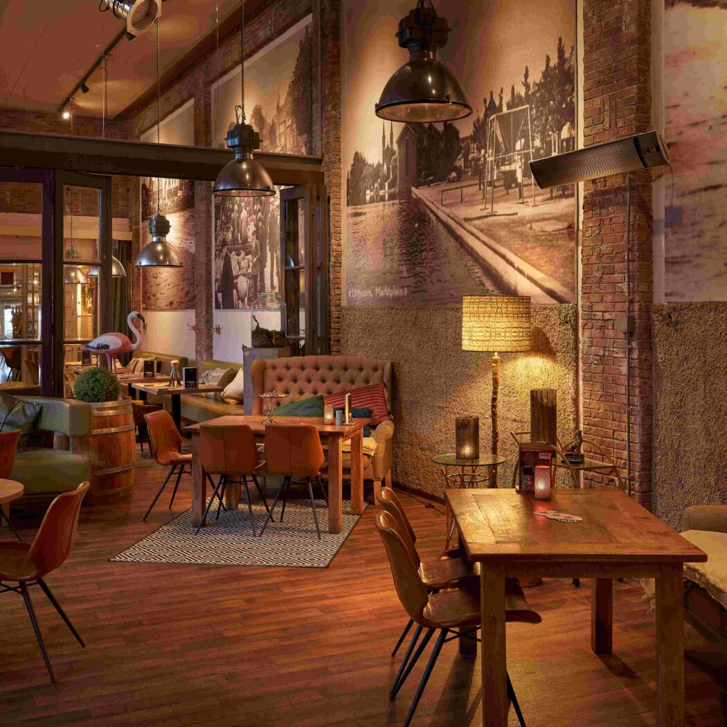Sfeervol restaurantinterieur in industriële stijl met houten vloeren, bakstenen muren, warme verlichting en grote zwart-wit muurschilderingen.