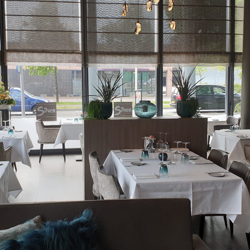 Interieur van Restaurant Silver met gedekte tafels, moderne inrichting en uitzicht op de straat door grote ramen.