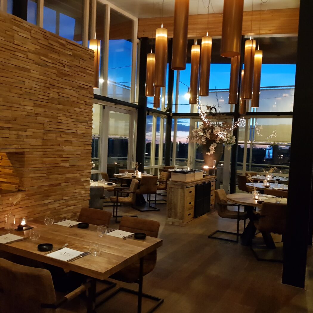 Warm verlicht restaurant met houten lambrisering, stijlvolle hanglampen en gedekte tafels bij schemering.