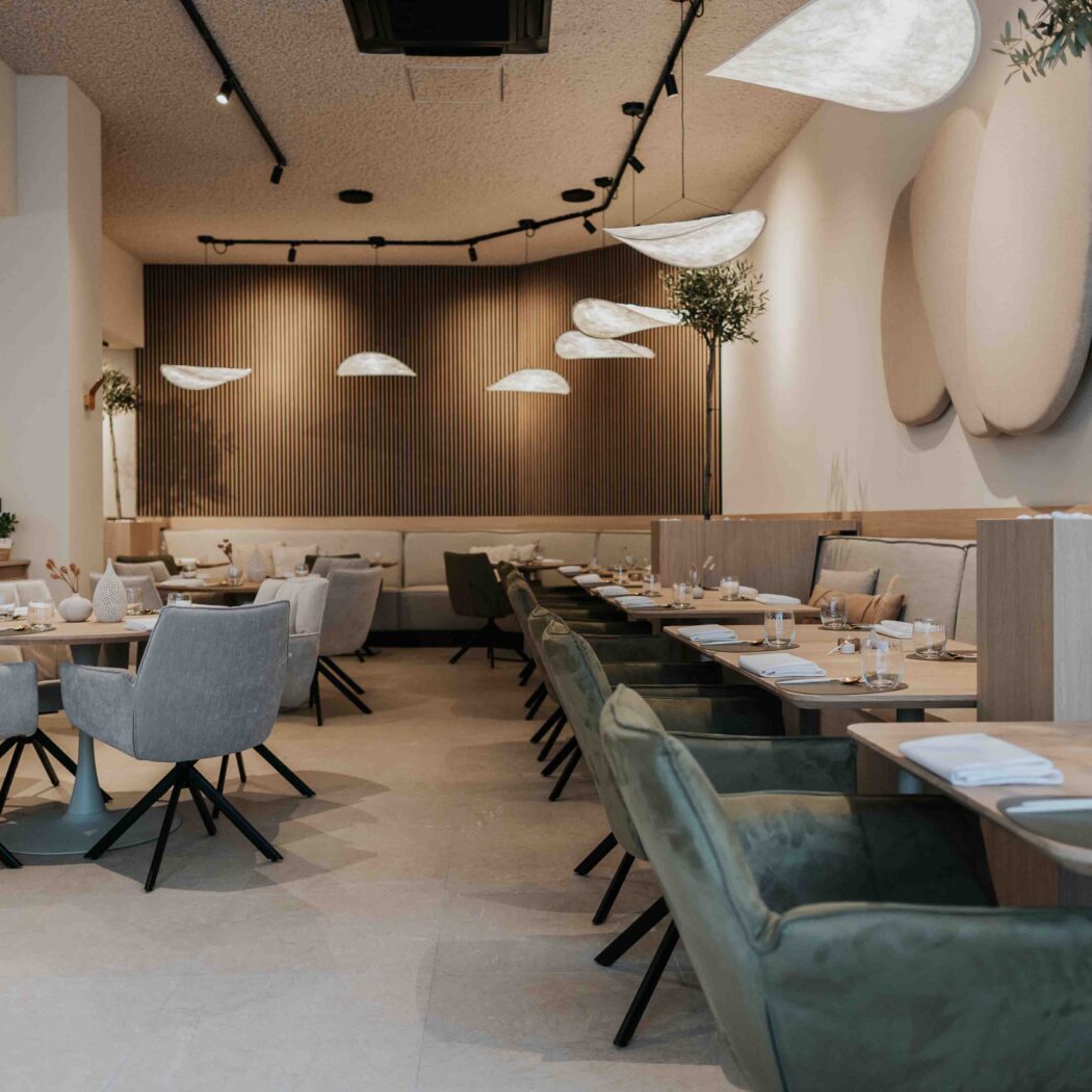 Modern restaurantinterieur met houten tafels, gestoffeerde stoelen, houten lattenwand en organische verlichting.