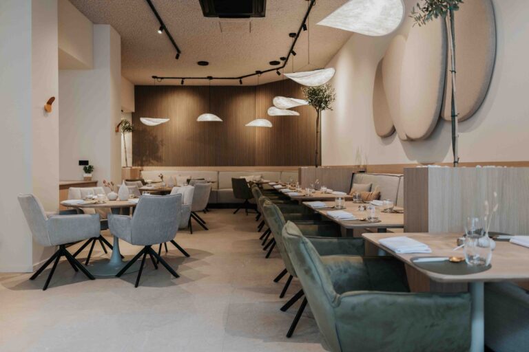 Modern restaurantinterieur met houten tafels, gestoffeerde stoelen, houten lattenwand en organische verlichting.