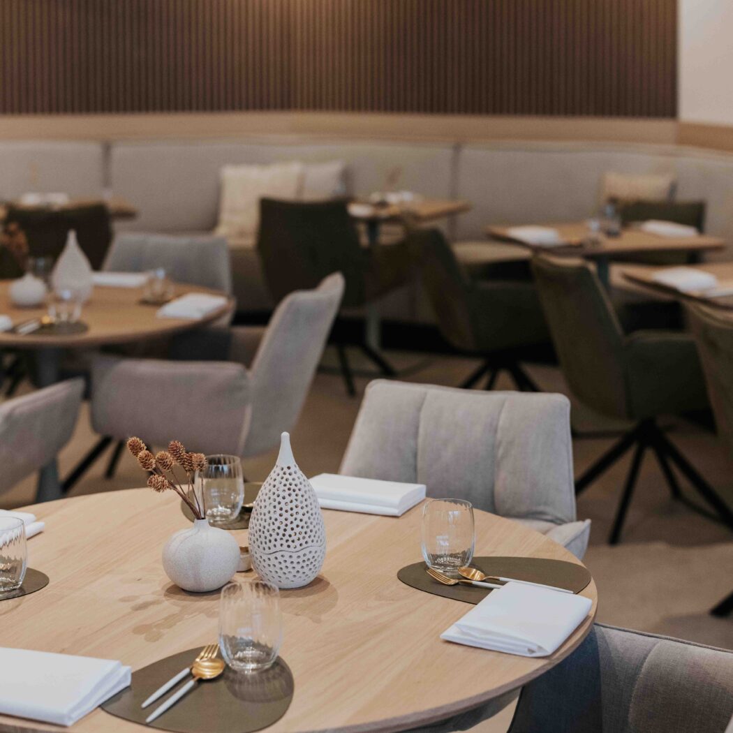 Ronde houten tafel gedekt met bestek en glaswerk, met decoratieve vazen, in een modern restaurant.