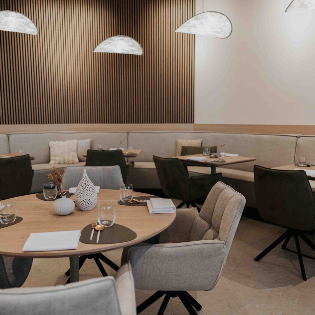 Stijlvol, leeg restaurant met ronde houten tafels, comfortabele beige banken en houten lambrisering.