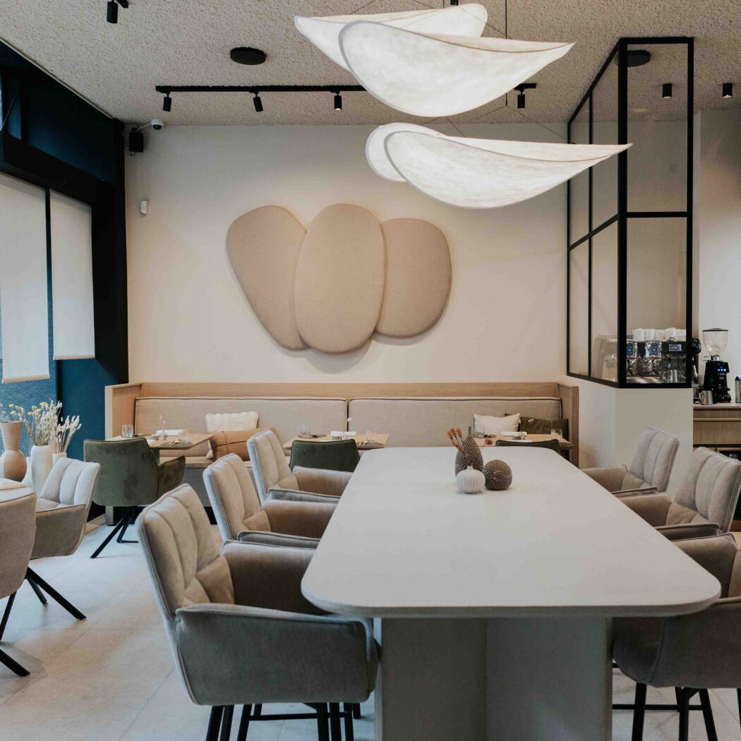 Stijlvolle restaurantruimte met lange witte tafel, comfortabele beige stoelen, banken en unieke cloud-vormige hanglampen.