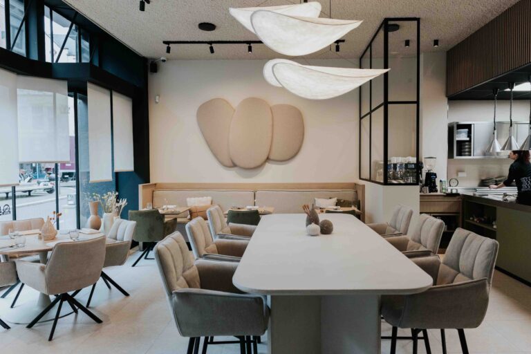 Stijlvolle restaurantruimte met lange witte tafel, comfortabele beige stoelen, banken en unieke cloud-vormige hanglampen.