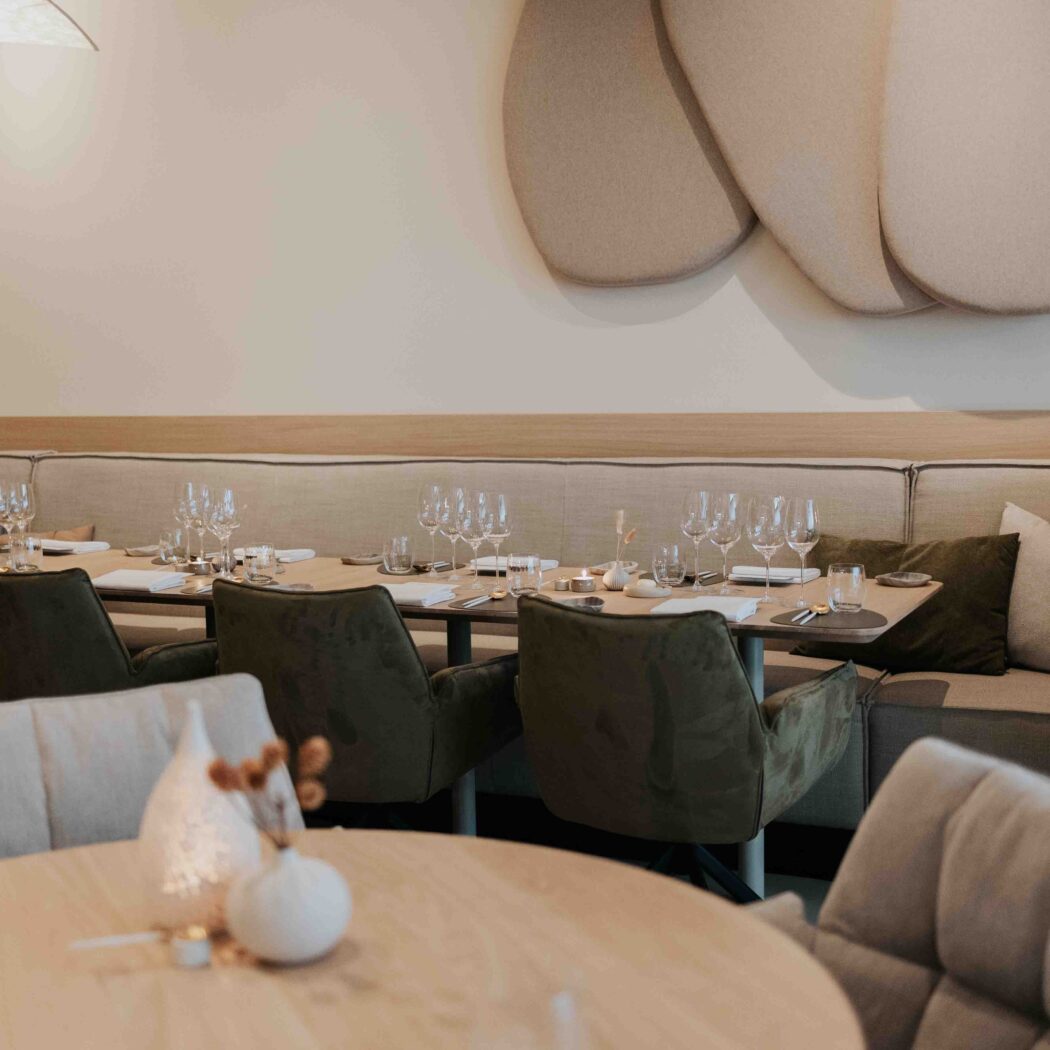 Sfeervol restaurantinterieur met gedekte houten tafels, groene fluwelen stoelen en beige zitbanken.
