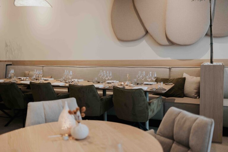 Sfeervol restaurantinterieur met gedekte houten tafels, groene fluwelen stoelen en beige zitbanken.