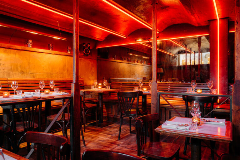 Intiem restaurantinterieur met houten meubilair, gedekte tafels en sfeervolle rode neonverlichting.