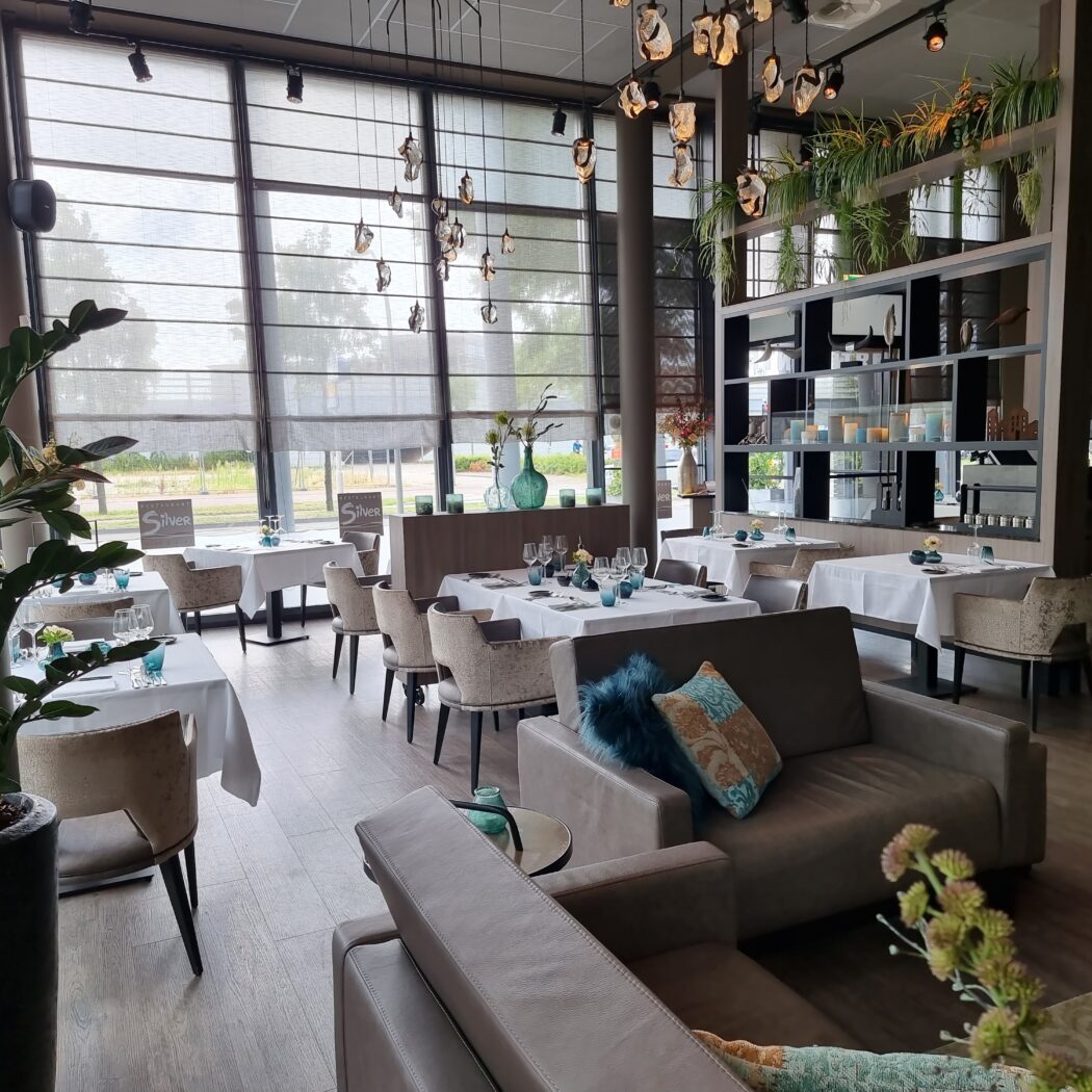 Modern restaurantinterieur met gedekte tafels, zitmogelijkheden en Restaurant Silver bordjes bij grote ramen.