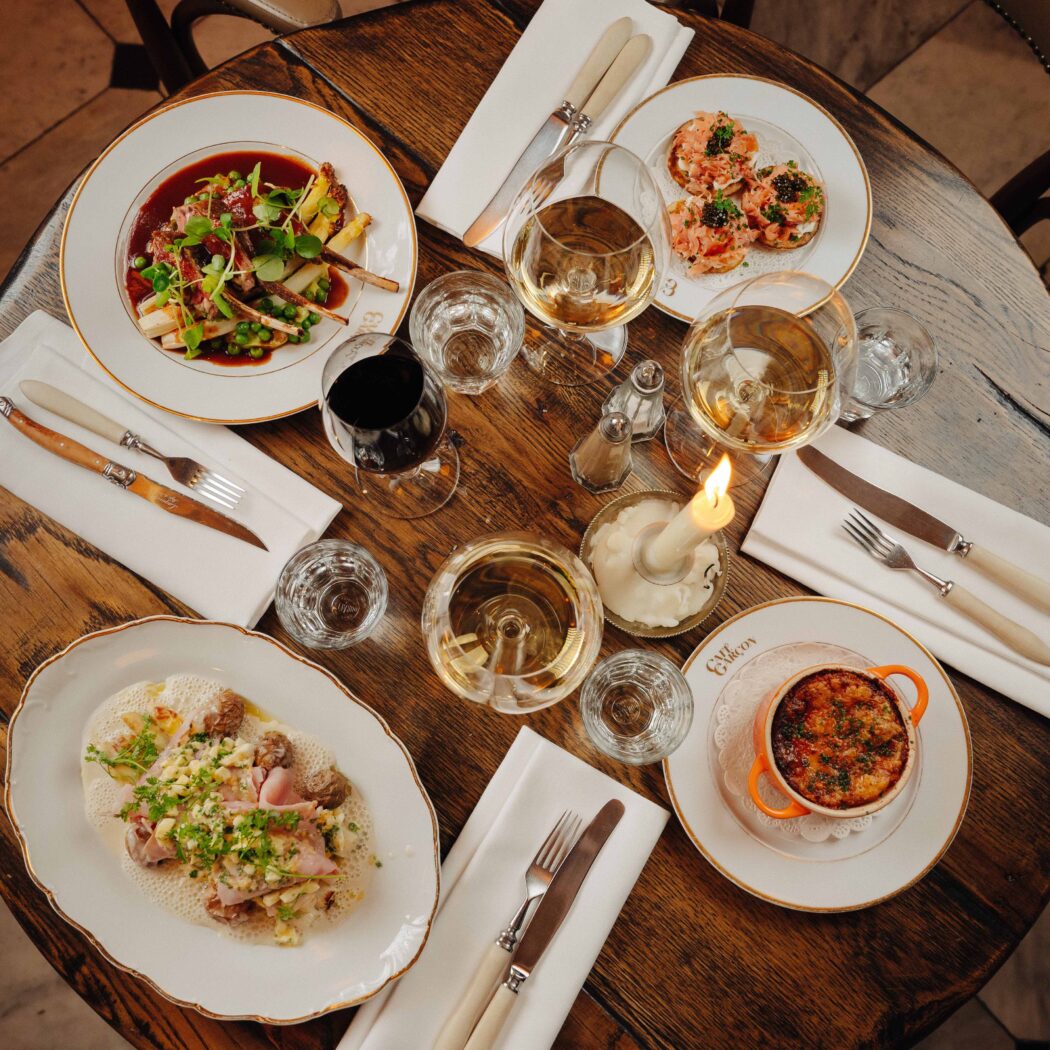 Bovenaanzicht van een sfeervol gedekte houten restauranttafel met diverse gerechten, wijnen en kaarslicht.