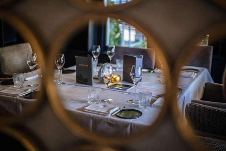 Elegante restauranttafel met wijnglazen, SHOW & TELL menukaart en gouden decoratie, gezien door een gouden spiegelrand.