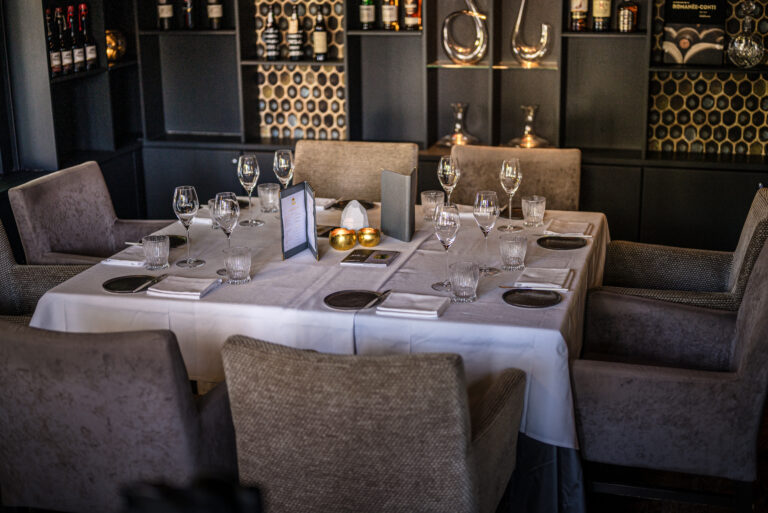 Een elegant gedekte restauranttafel met kristallen glazen, gouden kaarsenhouders en menus, omgeven door gestoffeerde stoelen.
