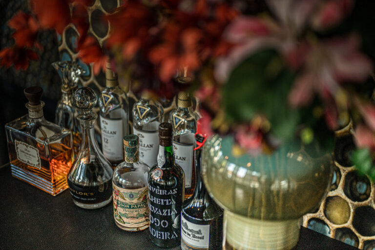 Flessen Macallan whisky, Taylors Port en Don Papa rum op een donkere ondergrond met rode bloemen.