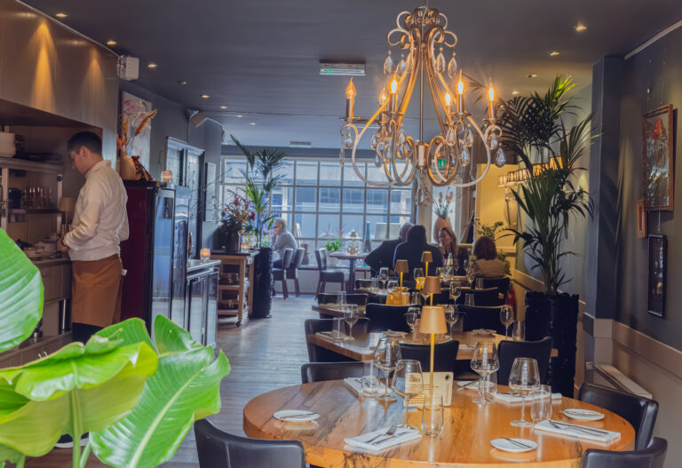 Warm verlicht restaurant met sierlijke kroonluchter, houten tafels met Bites menu, gasten en een kok aan een balie.