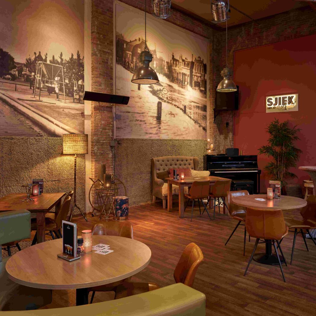 Gezellig restaurantinterieur met houten vloer, historische muurfotos, bakstenen muren, zitjes en een SJIEK eten & drinken bord.
