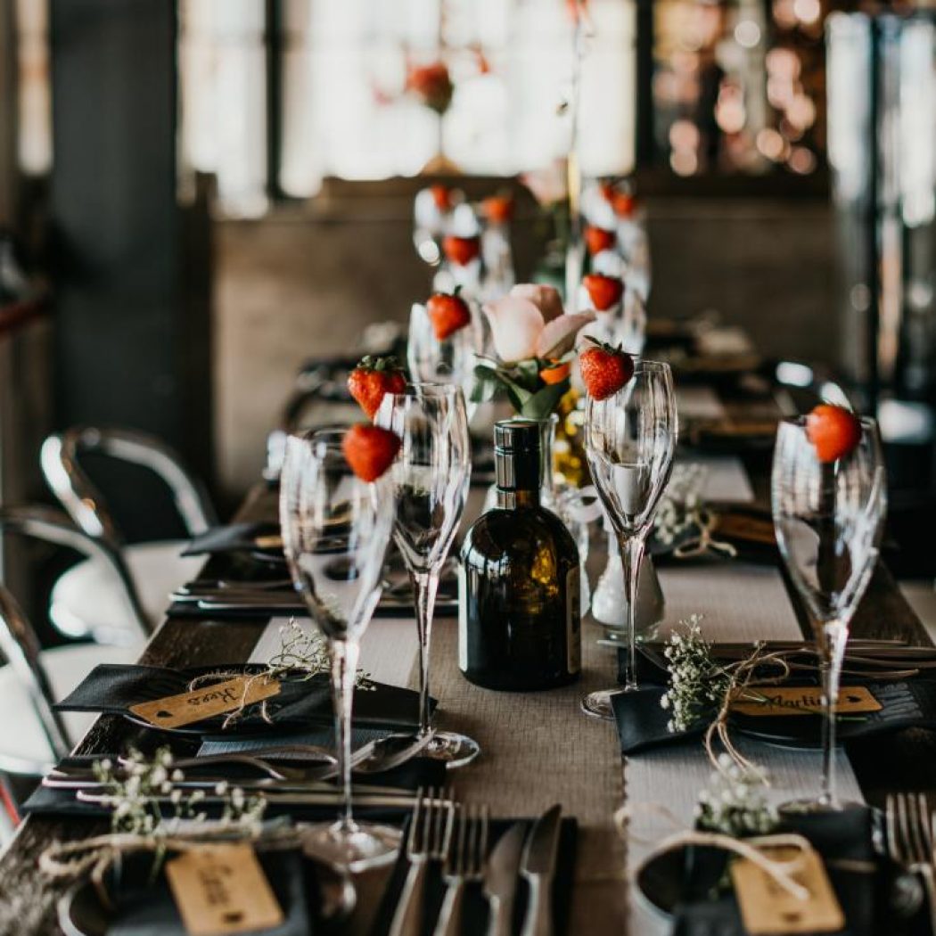 Feestelijk gedekte houten tafel met wijnglazen, aardbeien en bloemstukjes als decoratie.