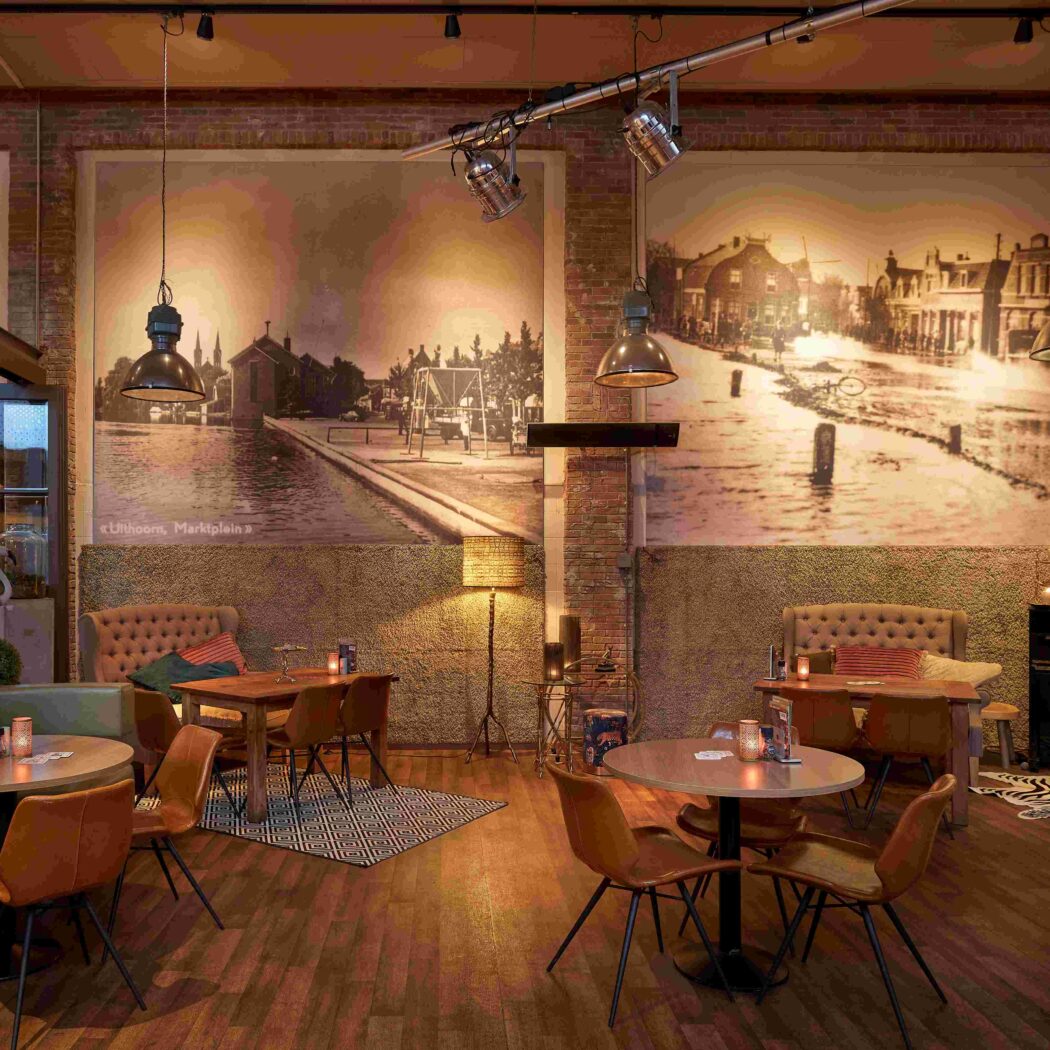 Industriële bar/restaurant met bakstenen muren, grote sepia wandfotos van Uithoorn, Marktplein en diverse zitjes.