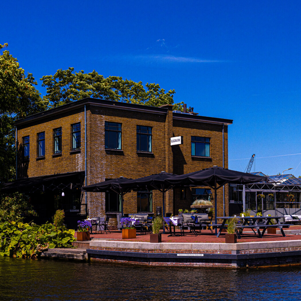 Restaurant GLASKERK, een bakstenen gebouw met terras en zwarte parasols aan het water op een zonnige dag.