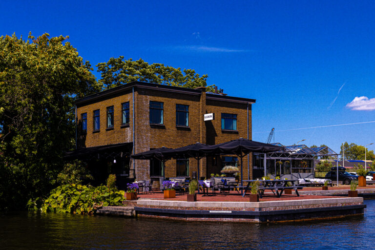 Restaurant GLASKERK, een bakstenen gebouw met terras en zwarte parasols aan het water op een zonnige dag.