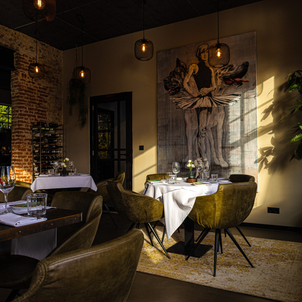 Sfeervolle restaurant eetzaal met gedekte tafels, olijfgroene stoelen en kunstwerk, badend in zonlicht.